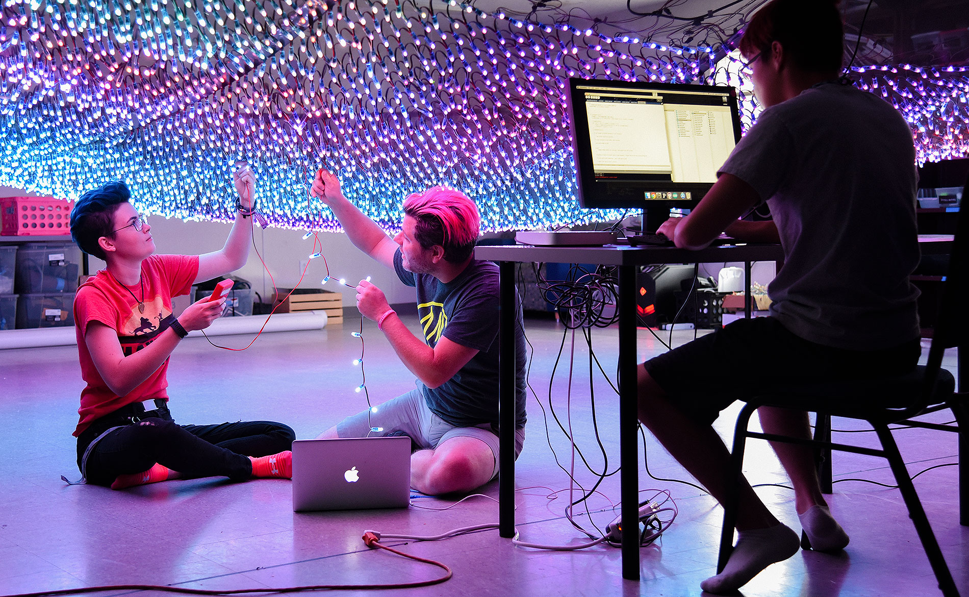 two students connecting wires to large light display and one student sitting at a computer