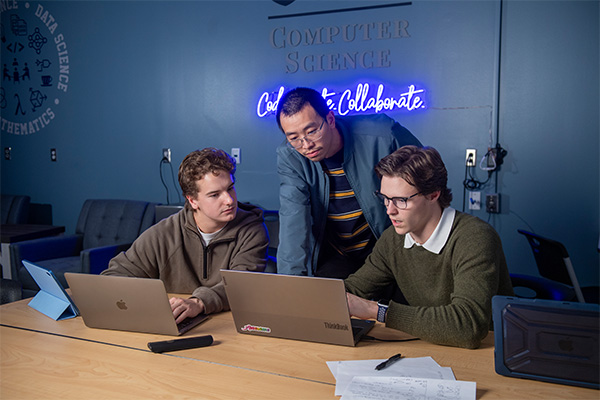 two students and professor looking at computer
