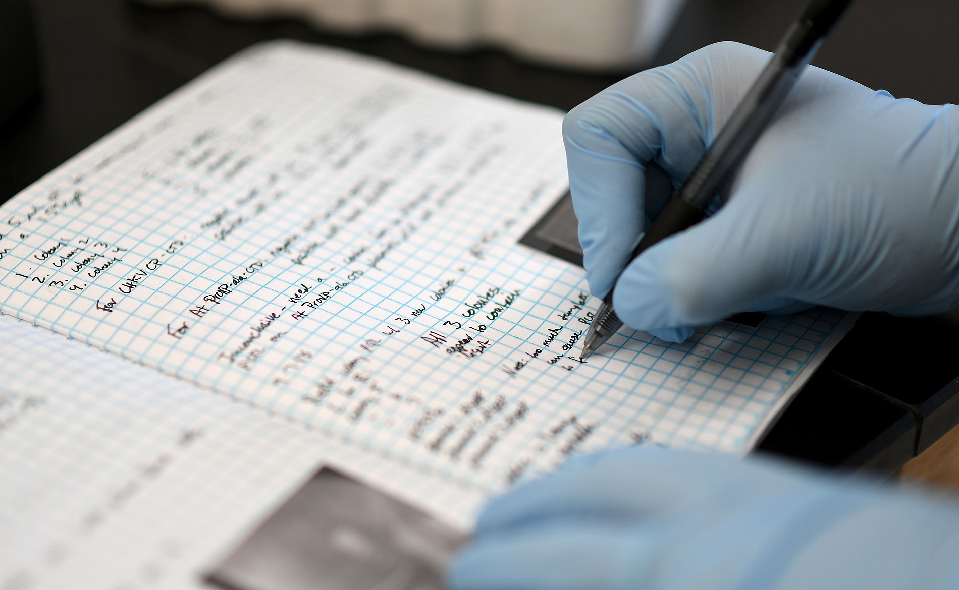 gloved hand writing on graph paper