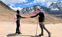 two students passing a camera between them in front of a mountainscape