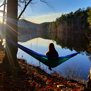girl sitting in a hammock watching the sunset over a lake