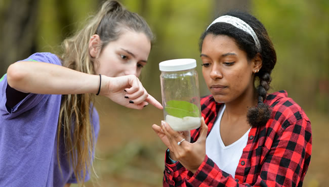 two female students examining plants and specimen in a glass jar