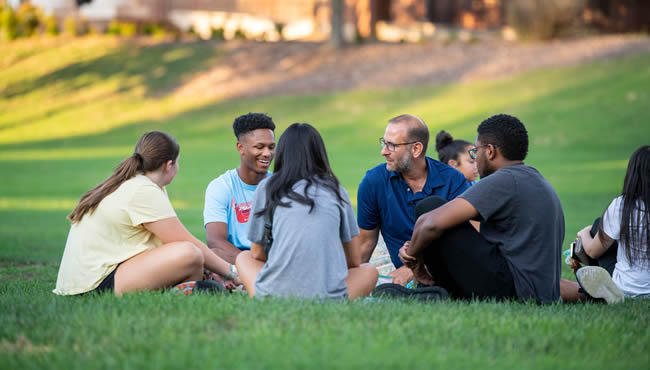 group of students and a professor chatting in a circle outside