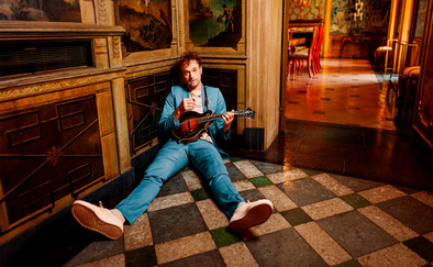 Chris Thile sitting on the floor playing an instrument