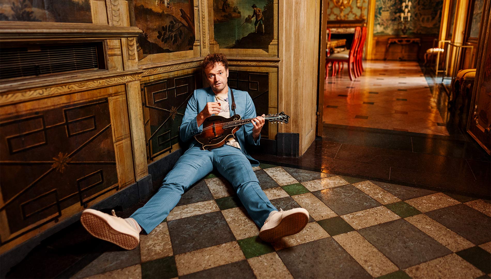 Chris Thile sitting on the floor playing an instrument