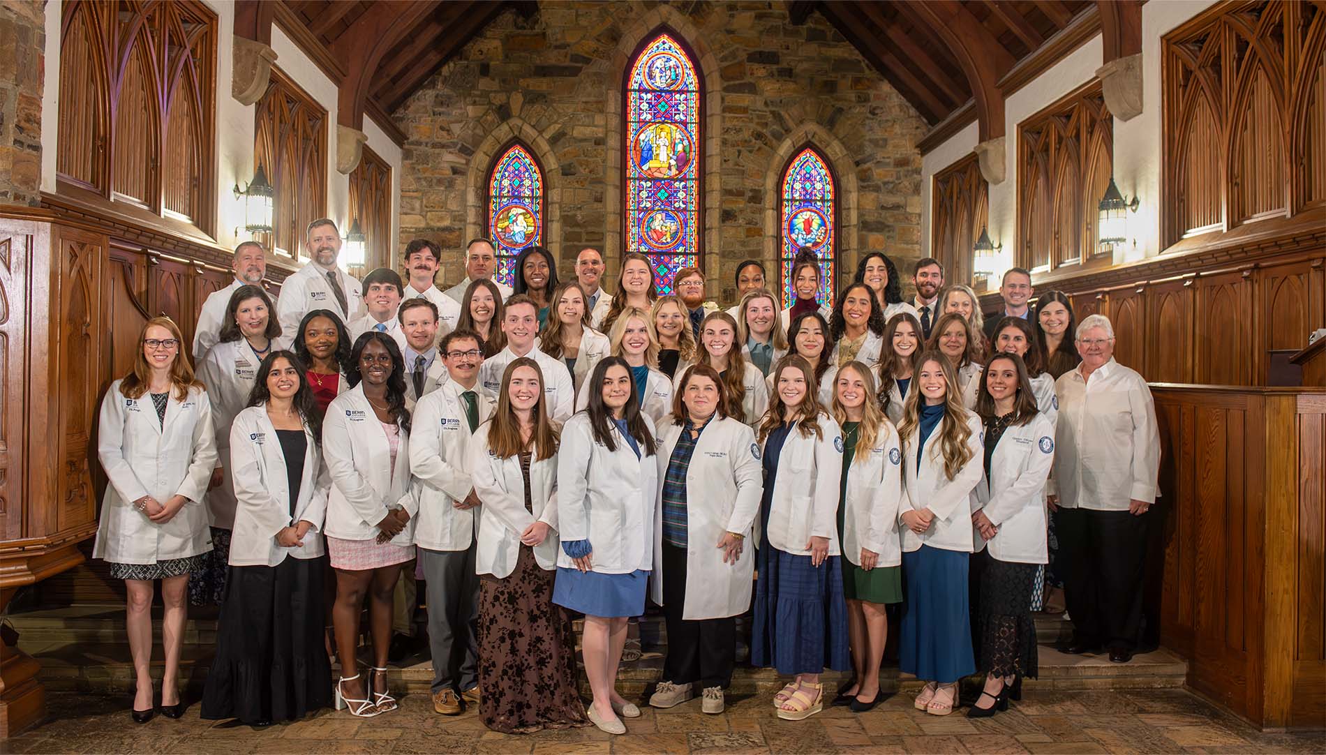Students and faculty on stage in white coats