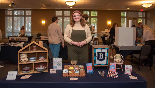 Allie Patterson behind a table covered in mixed-media artwork