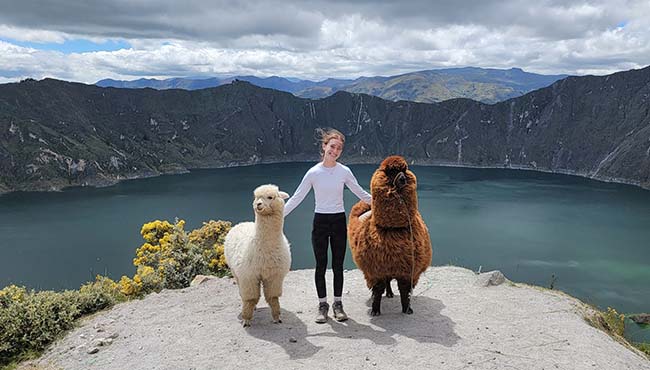 Sydney Summers standing on a cliffside with two alpacas