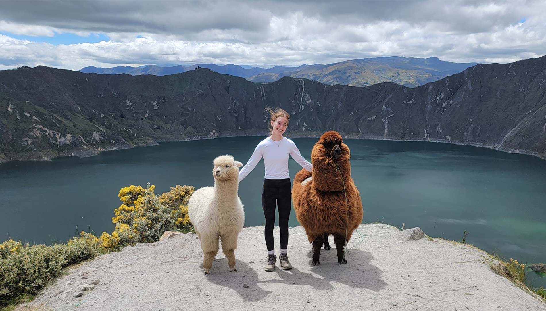 Sydney Summers standing on a cliffside with two alpacas