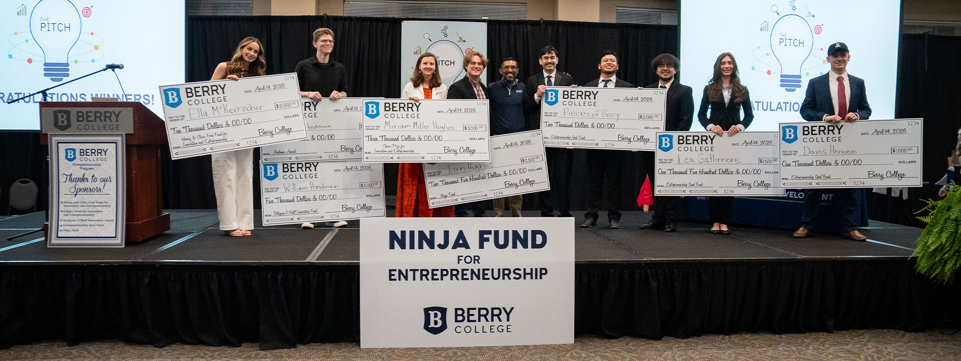 GRoup of students standing on stage holding oversized checks