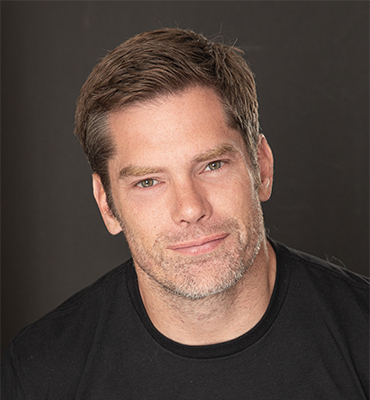 Dallas Jenkins smiling in front of a black background